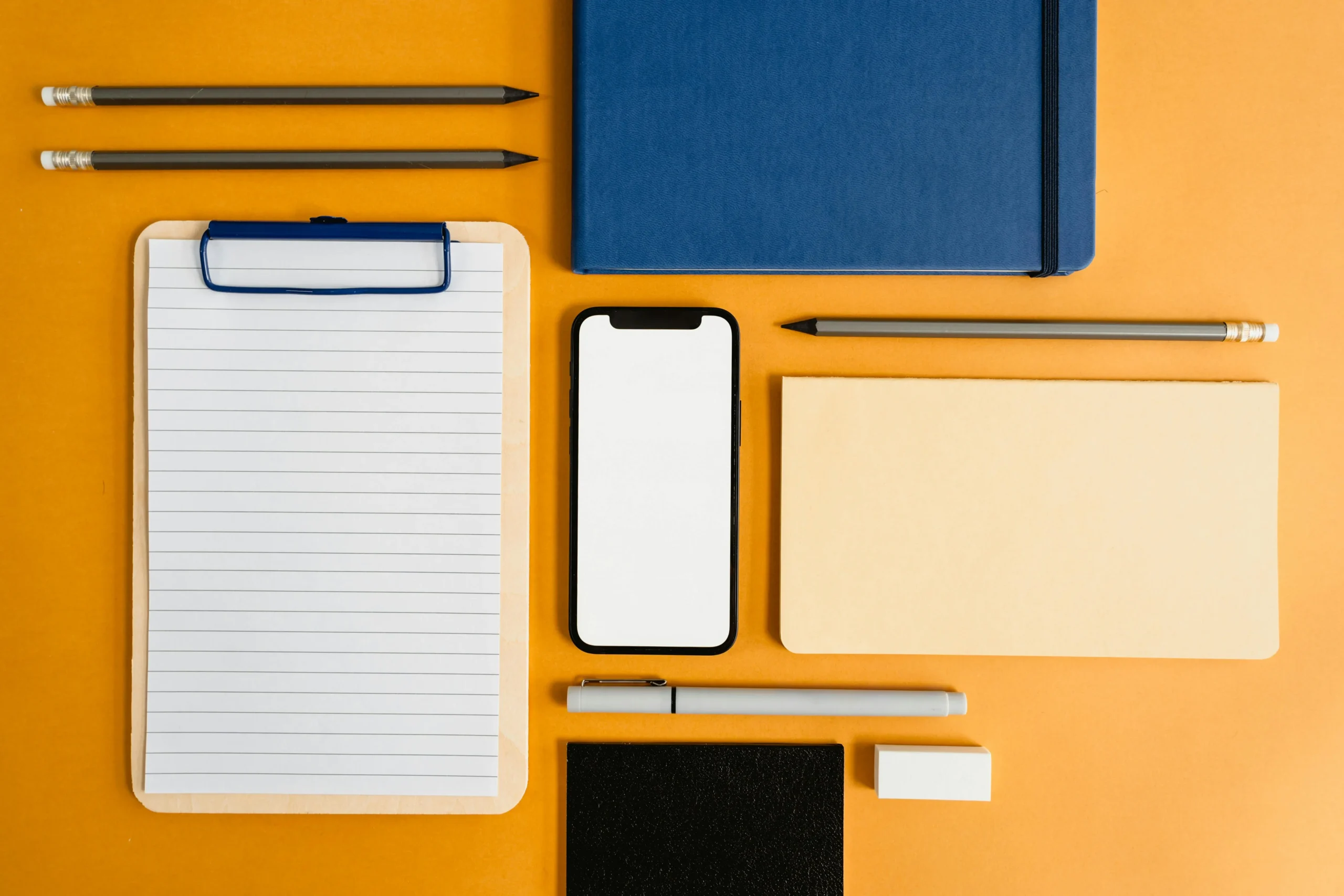 A desk table with pens, pencils, notepad, and cell phone on it.